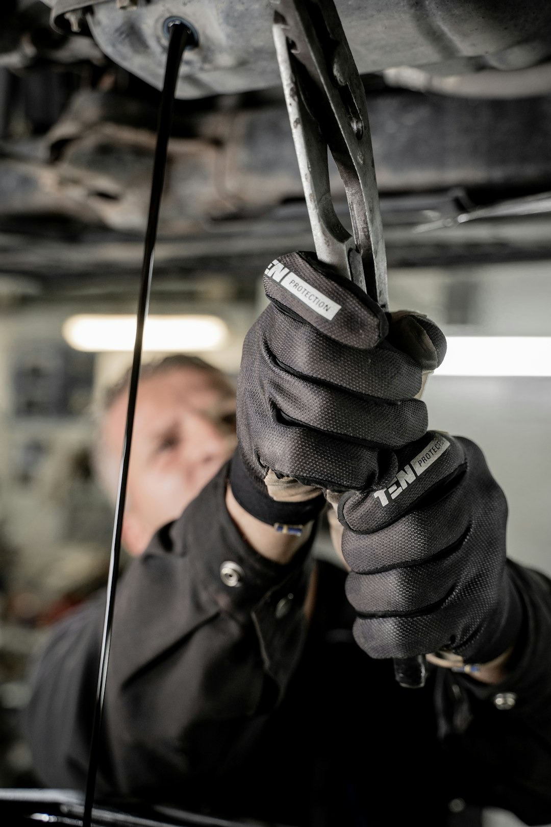 Mechanic in gloves changing oil under a car.