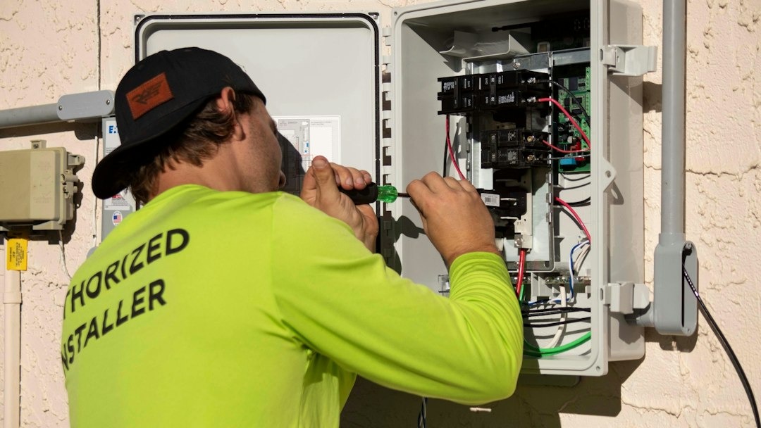 Man working on an electrical control panel with a screwdriver.